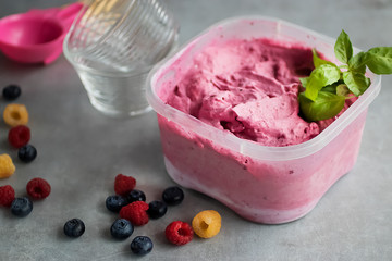 Homemade fresh berry ice cream with basil in  plastic box on gray background. Pink sorbet.