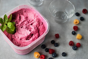 Homemade fresh berry ice cream with basil in  plastic box on gray background. Pink sorbet.