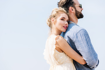Fototapeta na wymiar young beautiful blonde woman hugging bearded boyfriend with clear sky on background