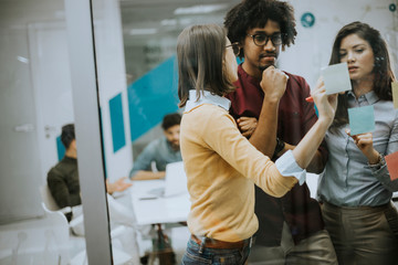 Young business people discussing in front of glass wall using post it notes and stickers