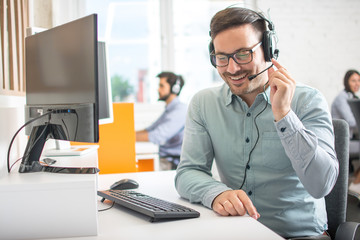Friendly customer support agent man with headset talking with client in call centre