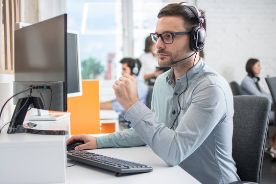 Handsome customer service support operator man with headphones and microphone using computer in call center