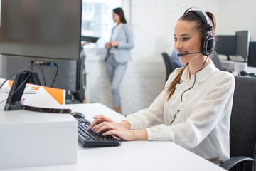 Friendly customer support operator with headset and microphone assisting to client in call centre