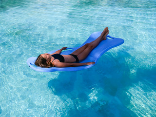 Pretty athletic sun tanned girl floating on a pool float in a swimming pool on vacation
