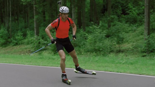 TRACKING Caucasian male professional biathlete roller skiing uphill on a forest track during mid-season practice in summer. ARRI Alexa Mini with Cooke S4 prime lenses RAW graded footage