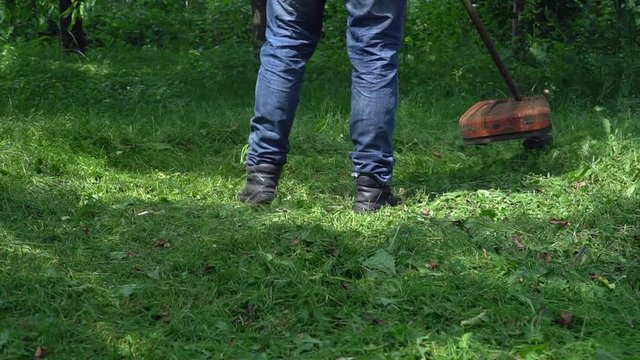 Close up. Man Gardener mowing lawn  with gasoline brush cutter, slow motion. Lawn mowing.