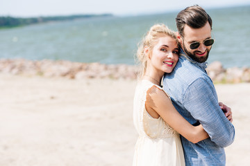 happy blonde woman hugging bearded smiling boyfriend at beach