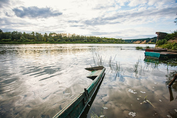 Naklejka premium abandoned old wooden fishing boat near pier in summer lake or river. beautiful summer sunny day or evening.