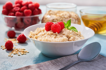 Homemade oatmeal with  fresh raspberries and organic honey for breakfast on a turquoise background.