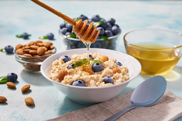 Homemade oatmeal with  fresh blueberry and organic honey for breakfast on a turquoise background.