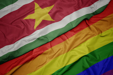 waving colorful gay rainbow flag and national flag of suriname.