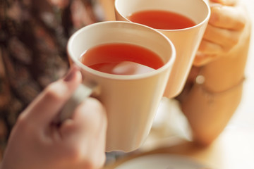 Close up photo of pretty women holding two mugs of delicious hot tea, drinking, smiling, in cozy morning cafe, selective focus, noise effect