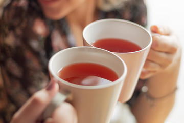 Close up photo of pretty women holding two mugs of delicious hot tea, drinking, smiling, in cozy morning cafe, selective focus, noise effect