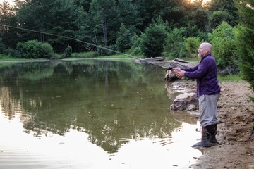 Peaceful Scene of Middle Aged Man Fishing on a Country Pond at Sunset with Golden filtered light reflected on pond