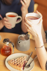 the process of drinking tea by girlfriends in a cafe. Photo of hands holding mugs with red fruit tea