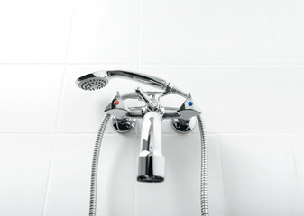 Chrome water tap and shower head in white wall bathroom