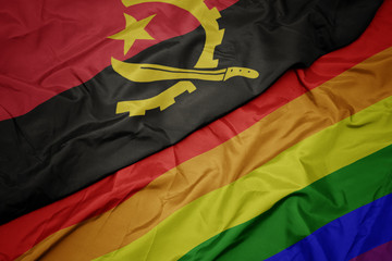 waving colorful gay rainbow flag and national flag of angola.