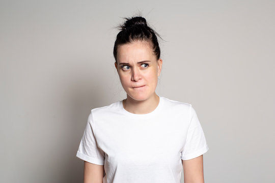 A pensive, doubting young woman pursed her lips and looks suspiciously to the side. Isolated on a white background.