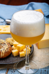 Cold belgian beer in glass served in cafe with variety of hard cheeses, tasty european food