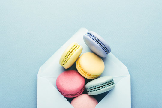 Colorful macarons in envelope on blue background.
