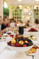 Grapes peaches gooseberry currant plum and other fruits on white vase on served table in restaurant