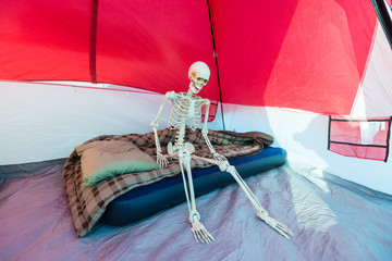 Skeleton sitting on blow up mattress in a tent while camping
