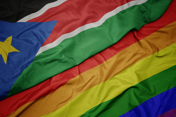 waving colorful gay rainbow flag and national flag of south sudan.