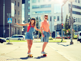 summer holidays, extreme sport and people concept - happy teenage couple riding short modern cruiser skateboards on city street