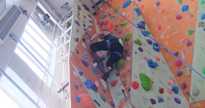 Woman climbing a dihedral on plastic holds, top rope - focus on foot placement. Looking up point of view.