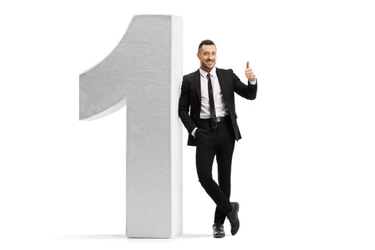 Young man in a black suit and tie leaning on number one and showing thumbs up