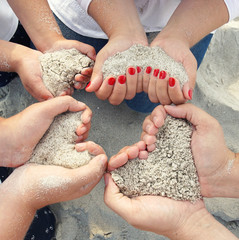 Familie formt Herzen mit Sand in den Händen