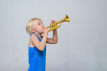 Little cute blond boy playing toy trumpet on light background