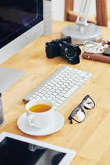 Glasses, cup of green tea, computer and digital camera on wooden table of creative project manager