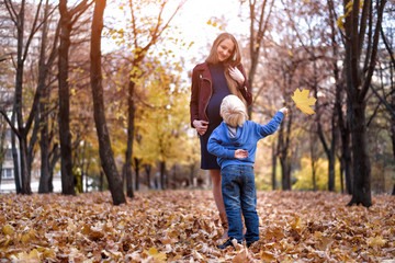 Little blond boy hid behind a yellow leaf. Wants to give mom. Autumn park on the background