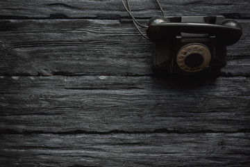 Black old rotary phone on a black wooden table flat lay background with copy space. Contact us.