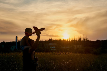 Fototapeta premium The son on his father’s shoulders launches the plane. The relationship of father and son.