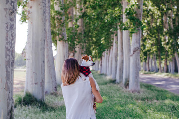 young beautiful woman holding her cute small dog on shoulder. outdoors. Love for animals concept and lifestyle outdoors