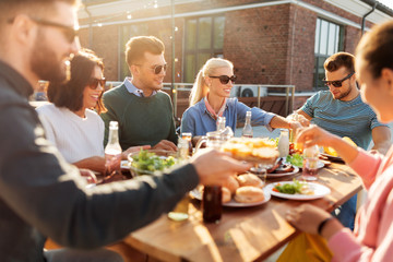 leisure and people concept - happy friends eating and drinking at barbecue party on rooftop