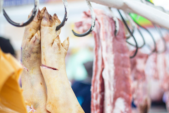 Pork legs with hooves and shank hanging on the counter: selective focus photo from the natural home market with meat horned animals
