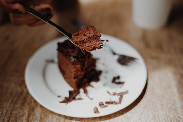 Hand holding brownie Chocolate cake with spoon to eat in modern cafe