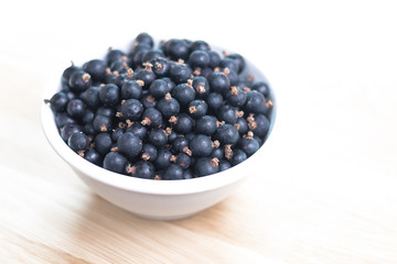 black currant berries in a white bowl, on table, white background