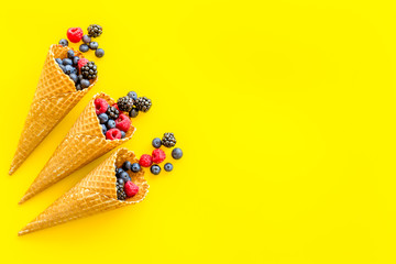 Fresh berries in waffle cones on yellow background top view mock up