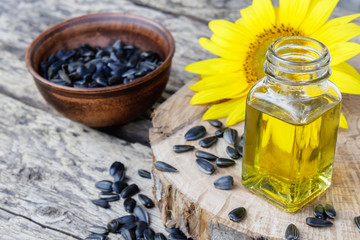 Sunflower oil and sunflower seeds in a bowl on a wooden background near fresh sunflower flowers. Organic and eco food.