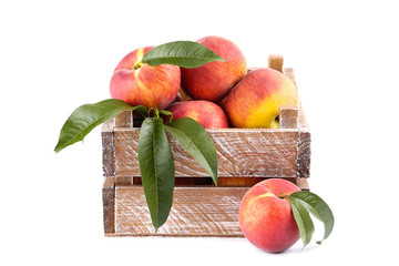 Fresh peaches with green leafs in crate isolated on white background