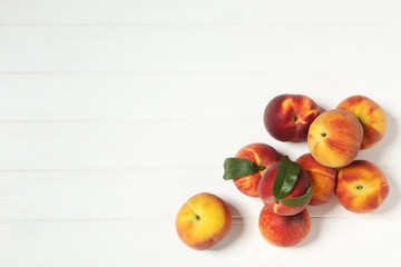 Fresh peaches with green leafs on white wooden table
