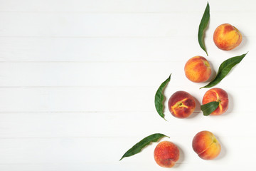 Fresh peaches with green leafs on white wooden table