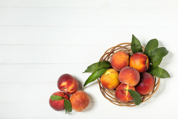 Fresh peaches with green leafs in basket on white wooden table