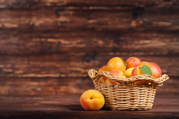Fototapeta na wymiar Sweet apricots in basket on brown wooden table