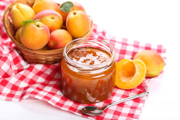 Jam in jar and apricots on white background