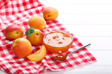 Jam in bowl and apricots on white wooden table